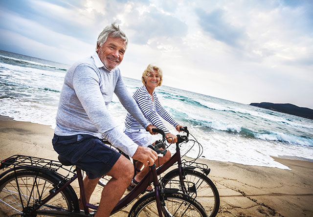 happy senior couple riding bikes on the beach